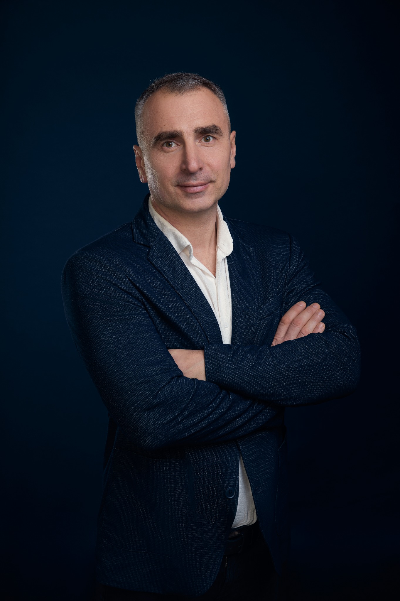 Portret agenta nieruchomości z Rogoża w granatowej marynarce, z założonymi rękami, na ciemnym tle. Profesjonalny wizerunek.