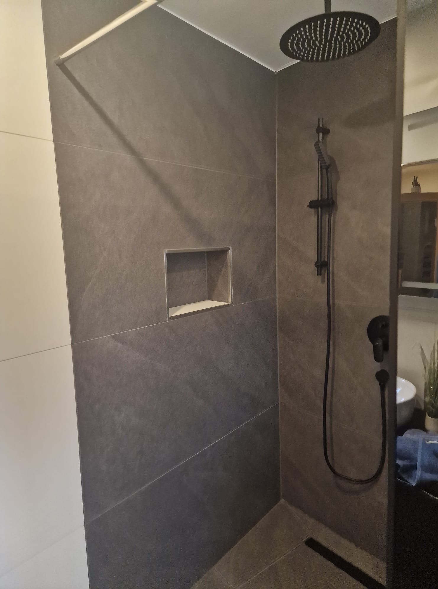 Nowoczesna kabina prysznicowa z szarymi płytkami imitującymi kamień, czarną armaturą i wnęką w ścianie, ukazująca minimalistyczny design wykończenia łazienki.