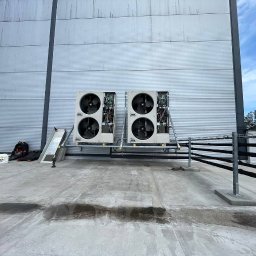 ICE VENTURO SPÓŁKA Z OGRANICZONĄ ODPOWIEDZIALNOŚCIĄ - Dwa agregaty wentylacyjne z otwartymi panelami na dachu budynku przemysłowego. Widoczne narzędzia i drabina. Instalacja wentylacji mechanicznej z rekuperacją.