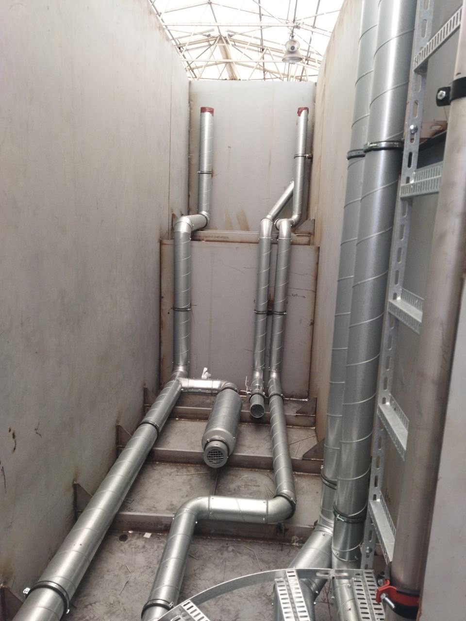 Wnętrze z widoczną instalacją rekuperacji: metalowe rury, kanały wentylacyjne, elementy montażowe. Widok z dołu na system wentylacji w przestrzeni technicznej.