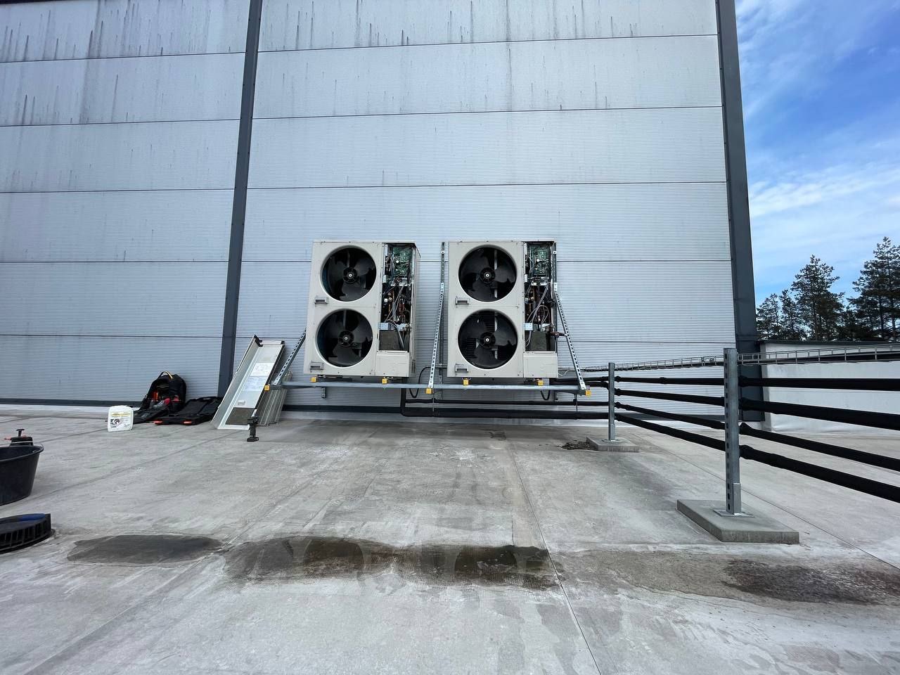 Dwa agregaty wentylacyjne z otwartymi panelami na dachu budynku przemysłowego. Widoczne narzędzia i drabina. Instalacja wentylacji mechanicznej z rekuperacją.