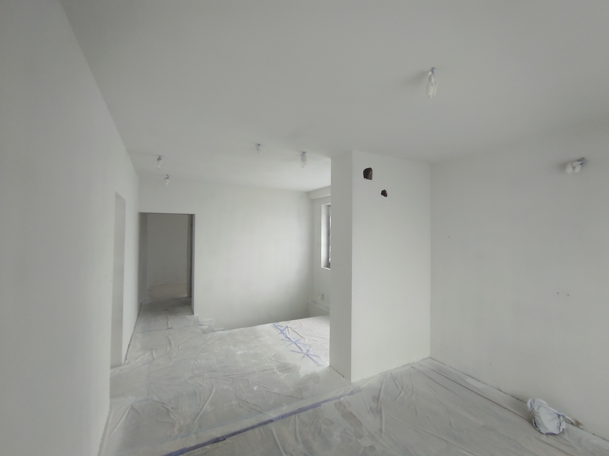 Białe, odświeżone wnętrze mieszkania po malowaniu. Podłoga zabezpieczona folią malarską. Widoczne otwory po gniazdkach elektrycznych.