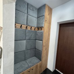 Bartek Prestigio - Zabudowa wnęki z siedziskiem i wieszakami, wykończona drewnopodobną płytą i tapicerowanymi panelami w odcieniach szarości. Funkcjonalne rozwiązanie do przedpokoju.