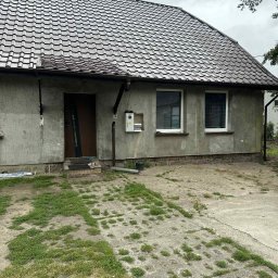 Termo - Tech Termomodernizacja Kamil Żurawowicz - Dom z brązowym dachem z dachówki karpiówki i surową elewacją, widoczny fragment betonowego podjazdu porośniętego trawą. Widok na budynek w pochmurny dzień.