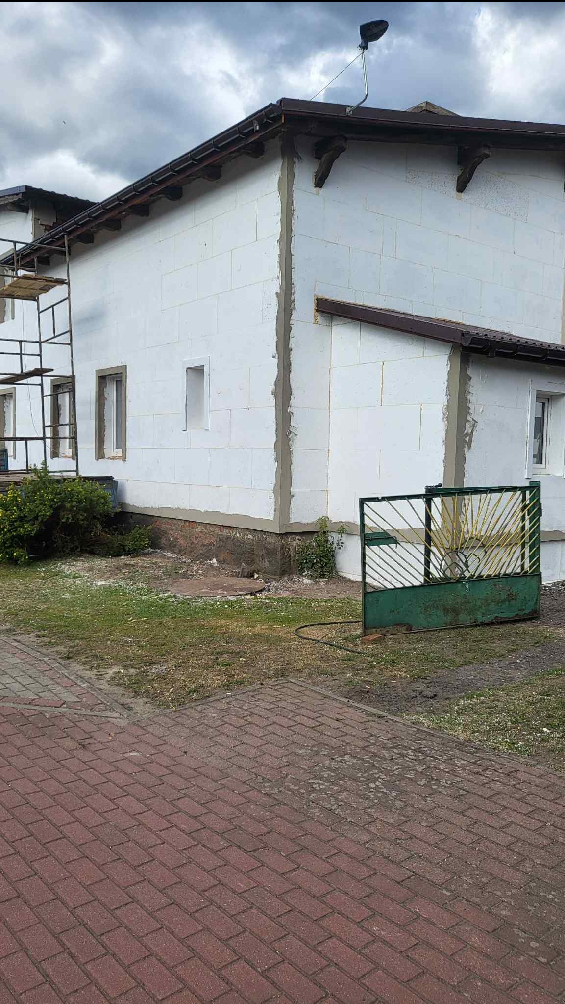 Dom w trakcie ocieplania: białe płyty izolacyjne na ścianach, widoczne rusztowanie i brama. Etap prac przed nałożeniem tynku.