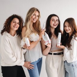 Foto Studio Izabela Godlewska - Cztery uśmiechnięte kobiety prezentują kosmetyki Solverx na białym tle. Różne typy urody, jasne ubrania, naturalne światło. Zdjęcie reklamowe.