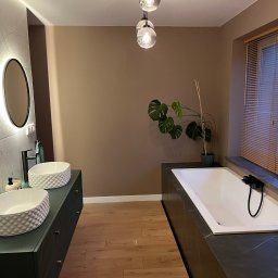 Filip Szumny Nieruchomości - Nowoczesna łazienka z dwoma umywalkami na szafkach w kolorze butelkowej zieleni, owalnymi lustrami z podświetleniem i wolnostojącą wanną.