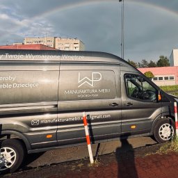 Wojciech Psiuk Manufaktura Mebli - Szary bus firmy meblarskiej z tęczą w tle. Na pojeździe widoczne logo i informacje o ofercie: kuchnie, szafy, garderoby, meble łazienkowe, biurowe i dziecięce.
