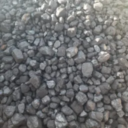 Kupa antracytu o nieregularnych kształtach, z widocznym metalowym elementem konstrukcyjnym w górnej części.  Światło podkreśla błyszczące powierzchnie bryłek.