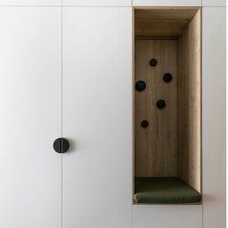 Balance - Biała szafa wnękowa z drewnianą wnęką z siedziskiem i czarnymi haczykami. Minimalistyczny design, jasne wnętrze, podłoga z paneli.