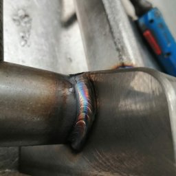 TOMASZ KULIGOWSKI DAR-TOM - Precyzyjne spoiny na metalowej konstrukcji, widoczne ślady po spawaniu i tęczowe zabarwienie metalu przy spawie. Detal z bliska ukazuje jakość wykonanej pracy.