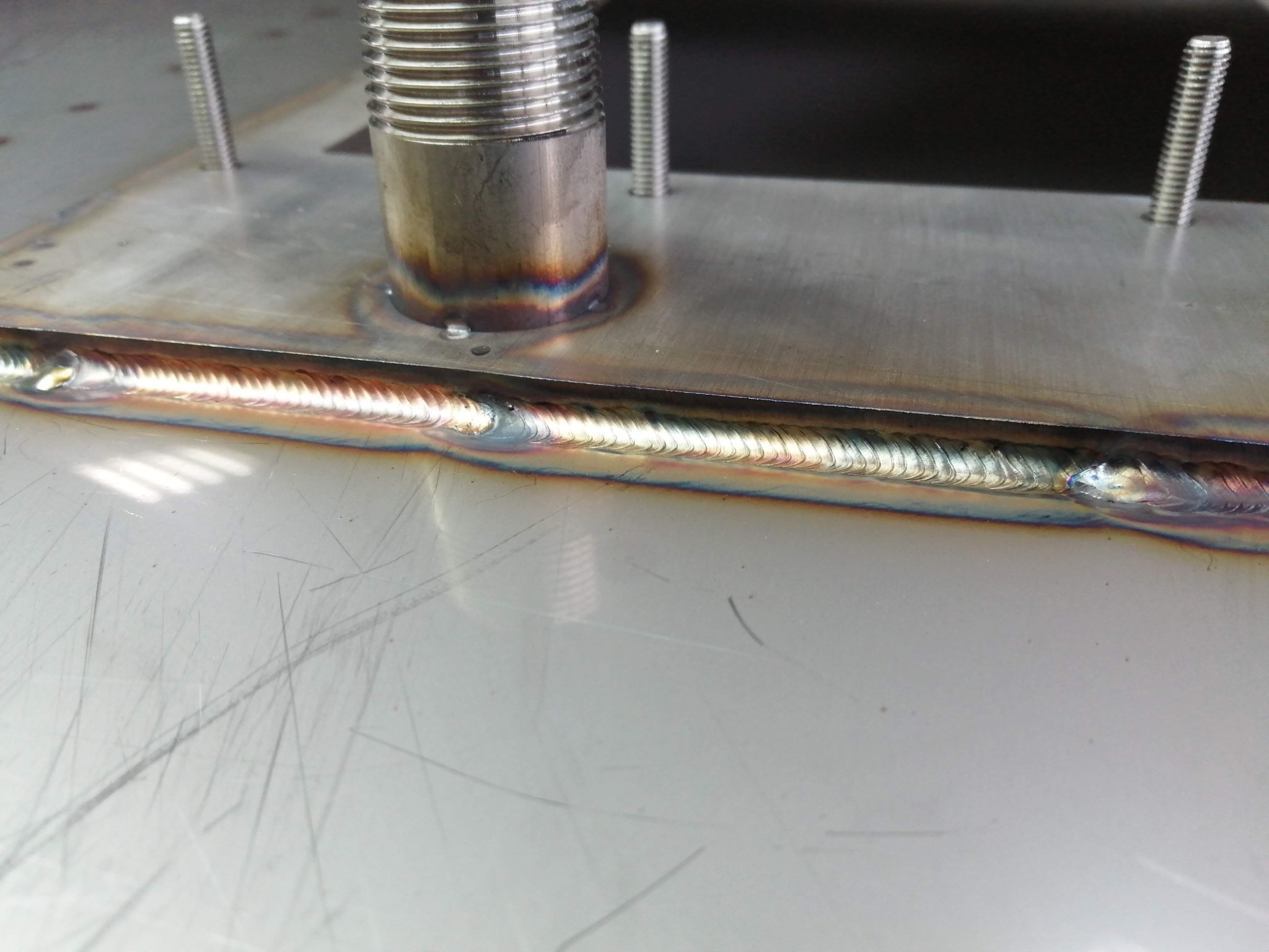 Metalowa płyta z precyzyjnym spoiną spawalniczą, widoczne śruby i gwintowany element. Detal wykonania z bliska, ukazujący jakość spawu.