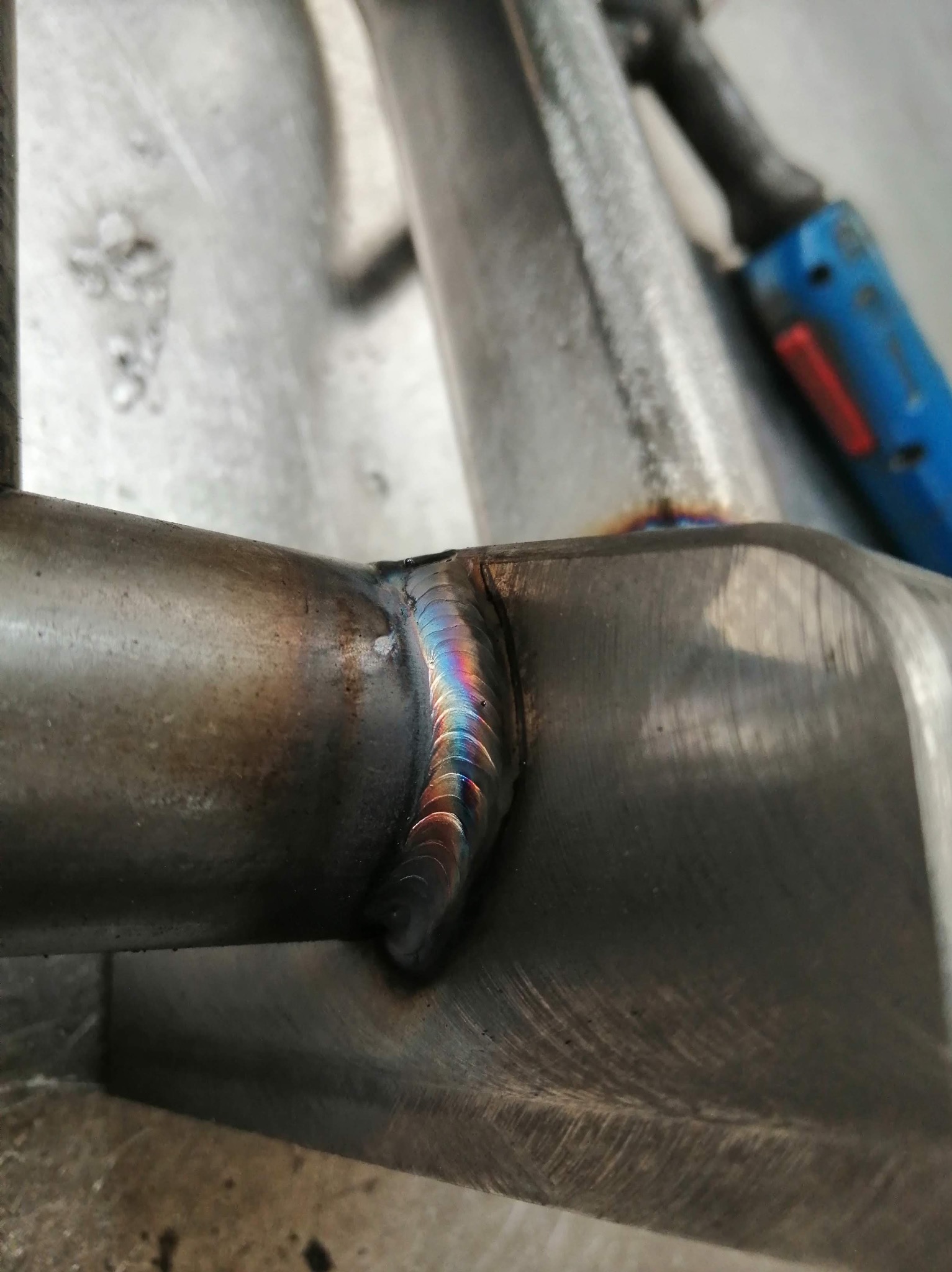 Precyzyjne spoiny na metalowej konstrukcji, widoczne ślady po spawaniu i tęczowe zabarwienie metalu przy spawie. Detal z bliska ukazuje jakość wykonanej pracy.