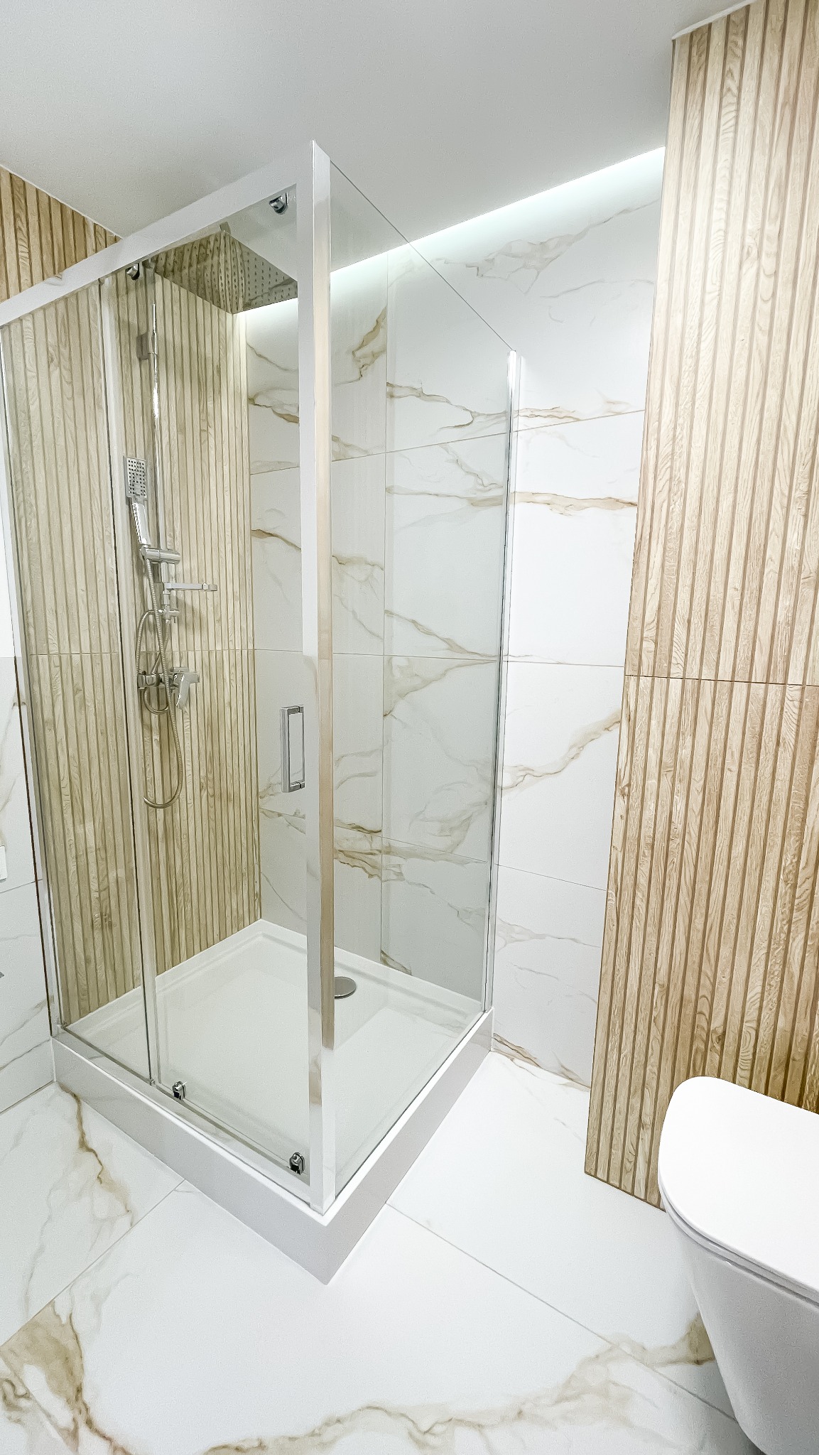 Nowoczesna kabina prysznicowa z deszczownicą, wykończona płytkami imitującymi drewno i marmur, w jasnej, przestronnej łazience. Minimalistyczny design.