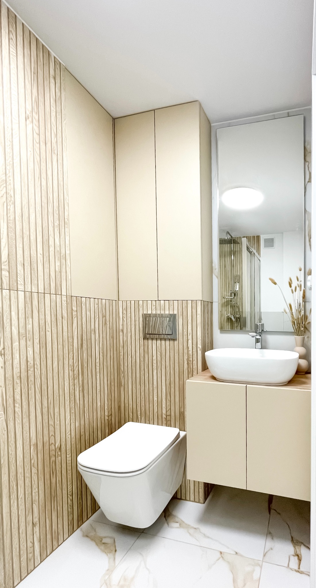 Nowoczesna łazienka w beżach i drewnie: wisząca toaleta, umywalka nablatowa, drewniana ściana z ryflowaniem, lustro. Minimalistyczny design, jasne wnętrze.