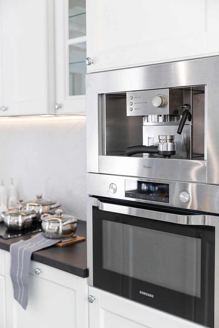 Nowoczesna kuchnia: zabudowany ekspres Whirlpool nad piekarnikiem Samsung, białe szafki, garnki ze stali nierdzewnej na blacie. Eleganckie wykończenie.