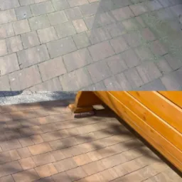 Zdjęcie 'przed i po' czyszczenia kostki brukowej. Górna część brudna, zielona od mchu, dolna czysta, w naturalnym brązowym kolorze, widoczny fragment konstrukcji drewnianej.