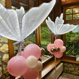 BALONOLA Aleksandra Daros - Dekoracja sali: podświetlane motyle na postumentach otoczone różowymi i brązowymi balonami, ustawione przy oknie z widokiem na zieleń. Kamienne wykończenie ścian.