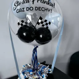 Ozdobny balon z napisem 'Sto lat Franku! GAZ DO DECHY!', z balonami w szachownicę i słodyczami w niebieskim pudełku, przewiązany błękitną wstążką.