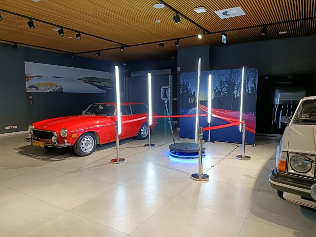 Czerwone Volvo kombi na obrotowej platformie, otoczone lampami LED i tłem z zimowym krajobrazem. Ekspozycja samochodów w muzeum, jasne oświetlenie.