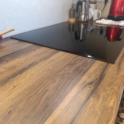 Effect cleaning - Błyszcząca płyta indukcyjna na drewnianym blacie kuchennym z widocznymi akcesoriami: czajnik, kawiarka i naczynia. Czysta powierzchnia gotowa do użycia.