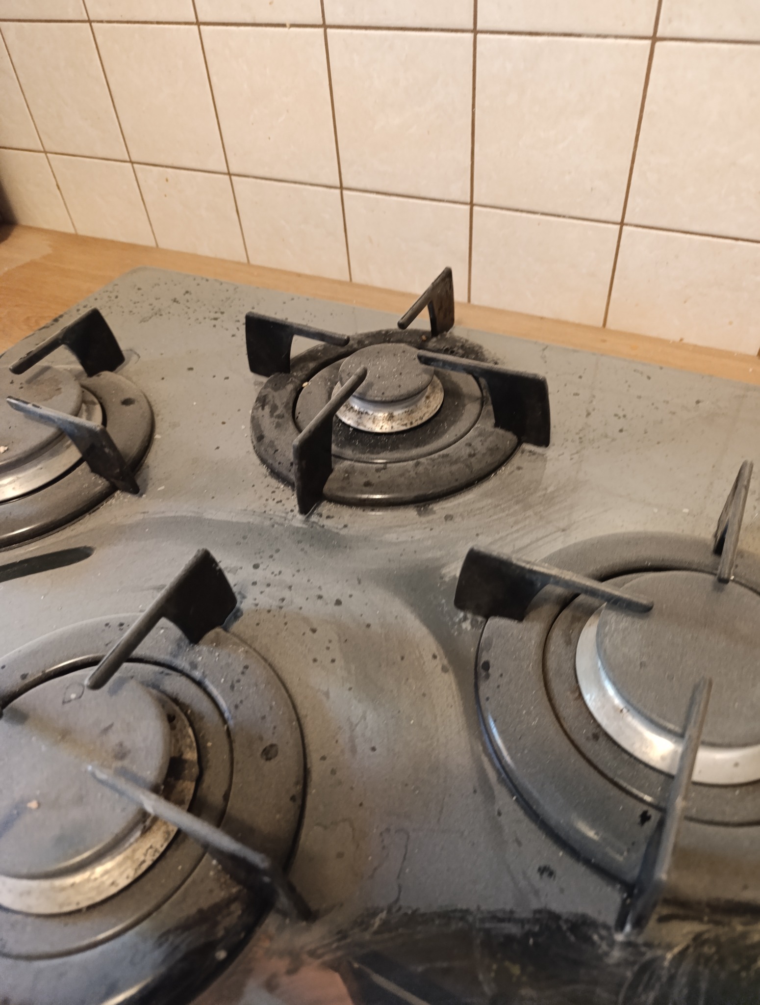 Zabrudzona, czteropalnikowa płyta gazowa z widocznymi zaschniętymi plamami i resztkami jedzenia, wymagająca czyszczenia, na tle jasnych płytek ściennych.