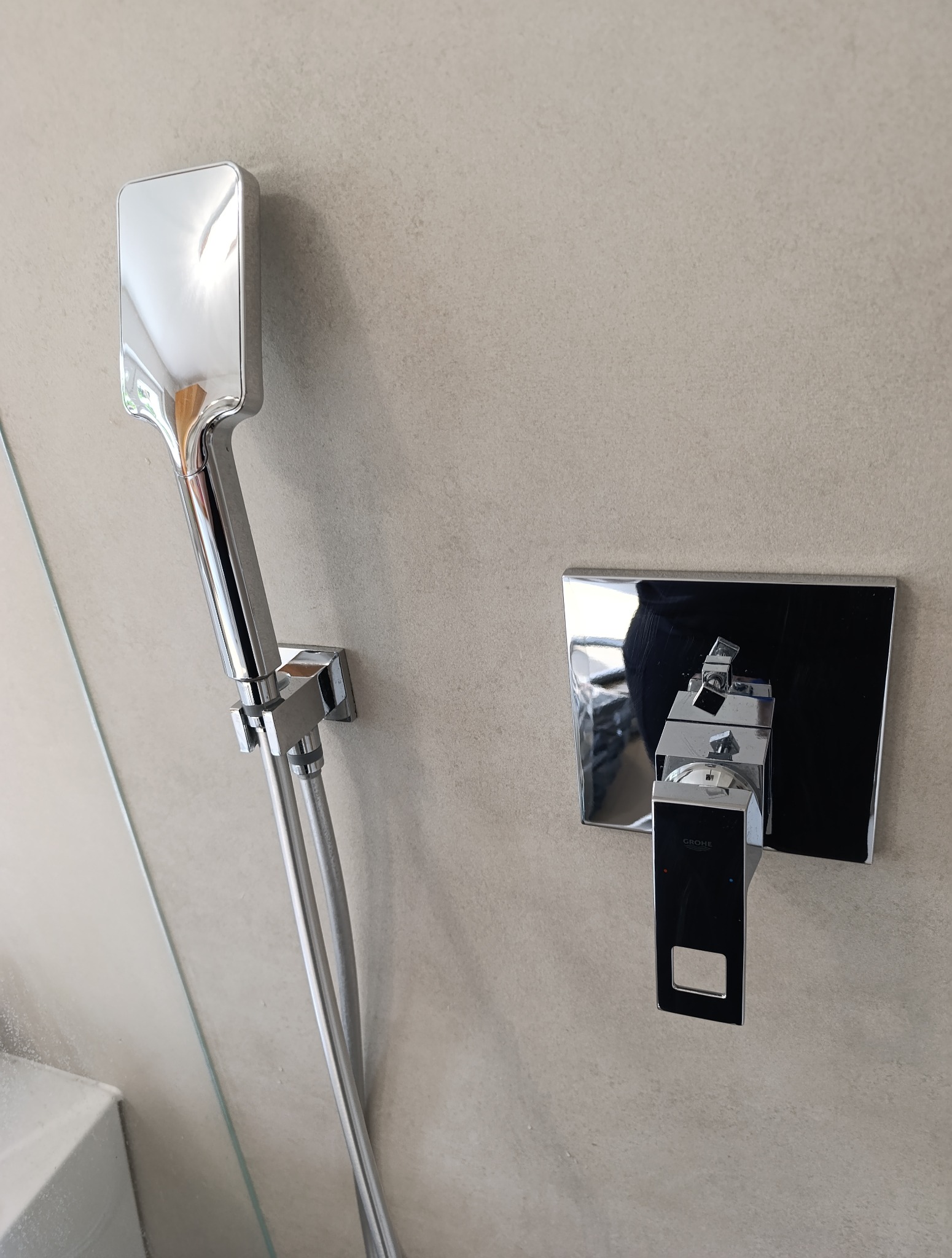 Bateria prysznicowa Grohe z kwadratową deszczownicą i minimalistycznym panelem sterowania na beżowej ścianie w nowoczesnej łazience.