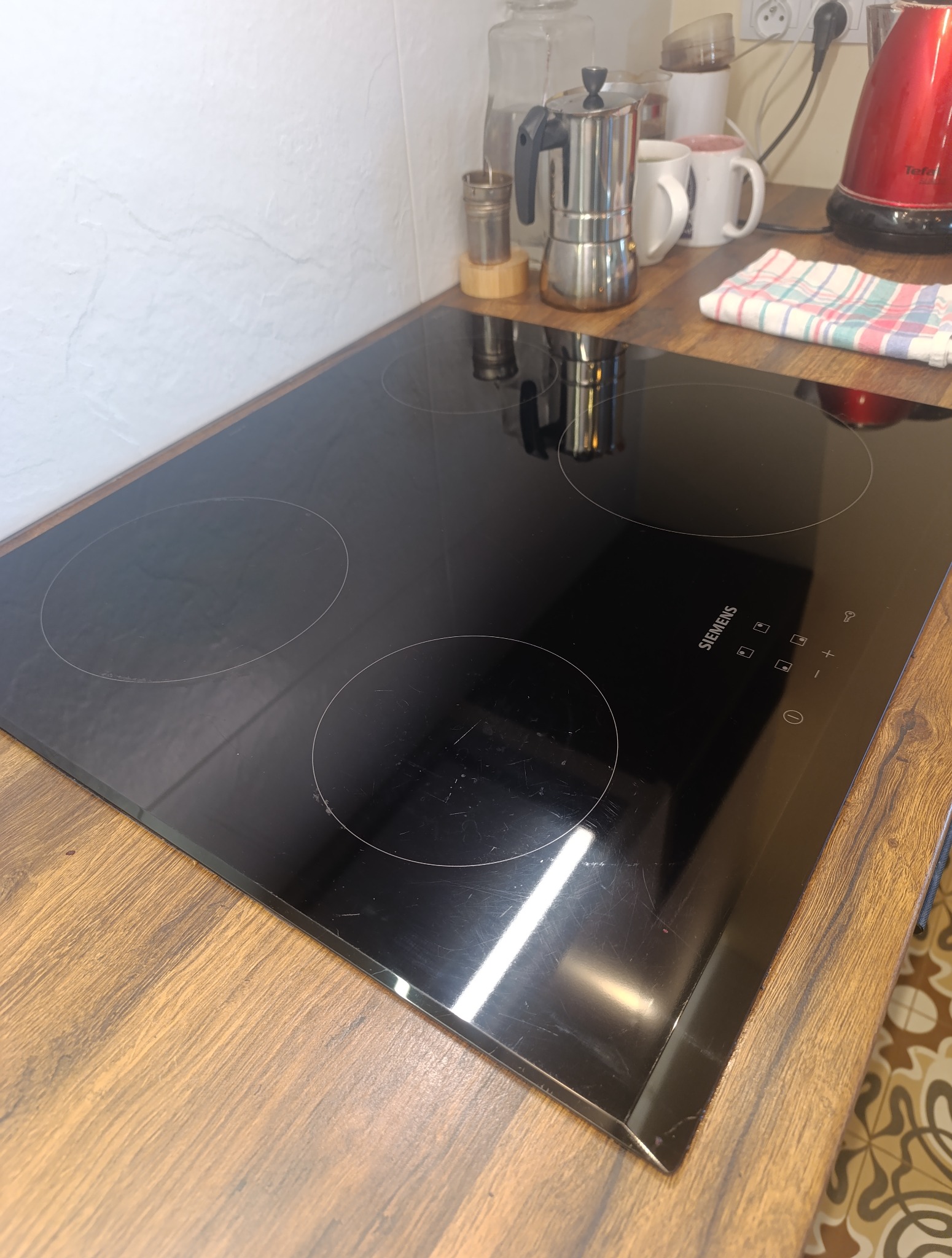 Błyszcząca, czarna płyta indukcyjna Siemens na drewnianym blacie kuchennym w Warszawie. Widoczne ślady użytkowania i odbicia.