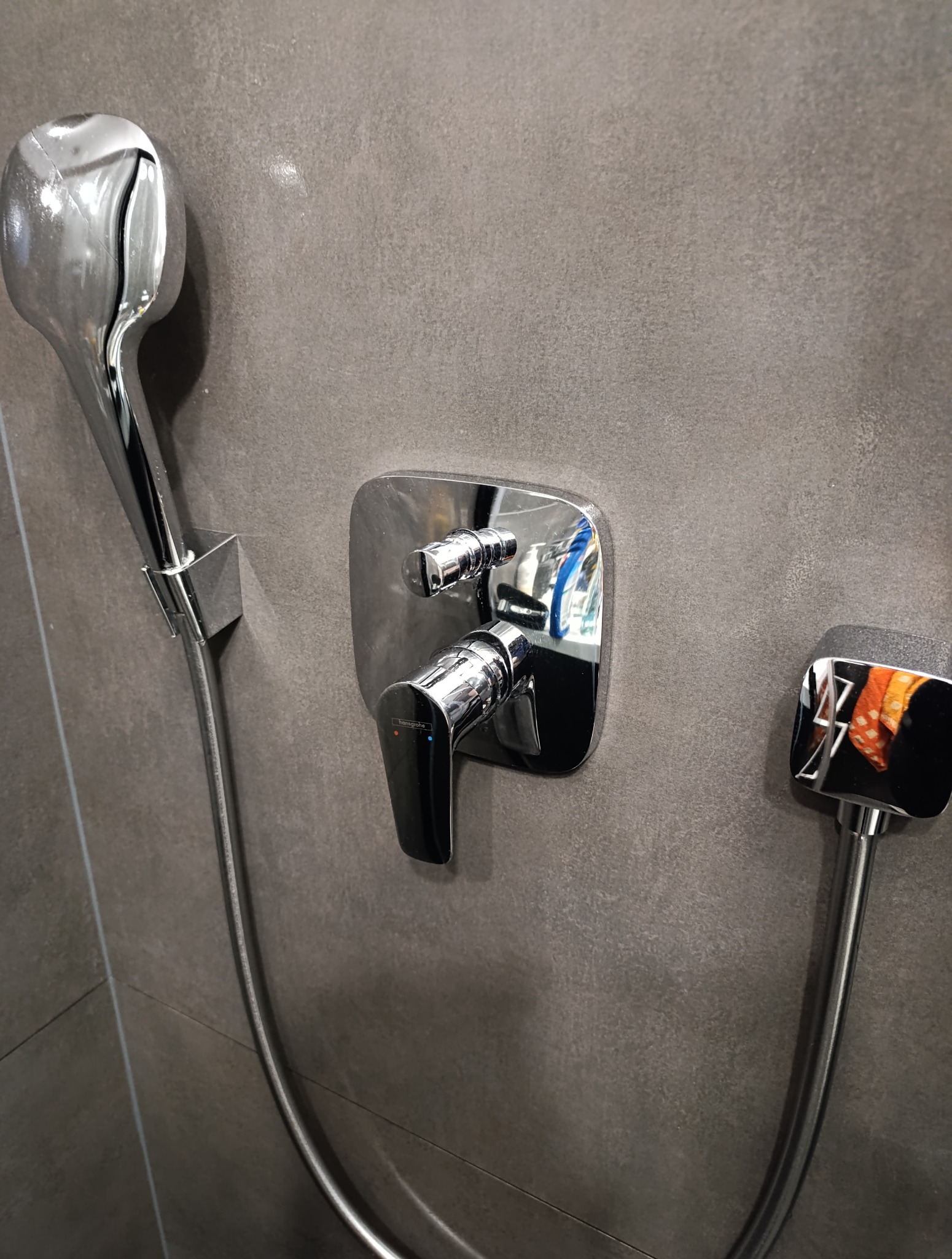 Bateria prysznicowa Hansgrohe w nowoczesnej łazience z szarą, matową płytką. Błyszczące chromowane wykończenie armatury.