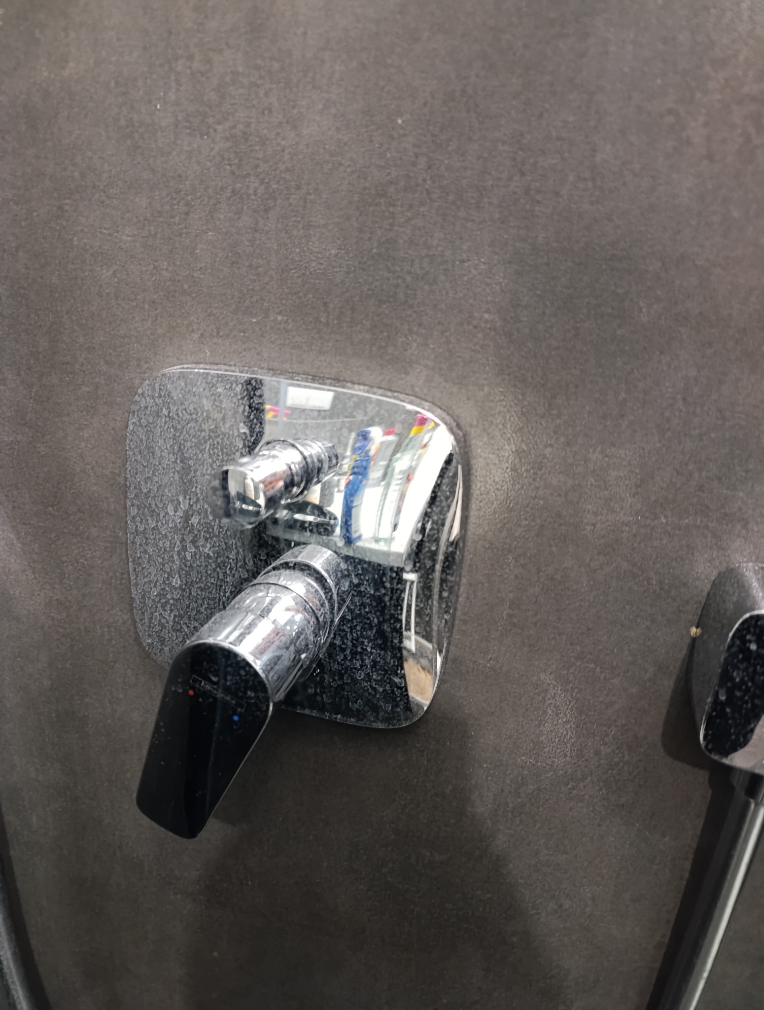 Zacieki na chromowanej baterii prysznicowej i ciemnej, matowej ścianie. Widoczne ślady po twardej wodzie. Powiększenie na detale.