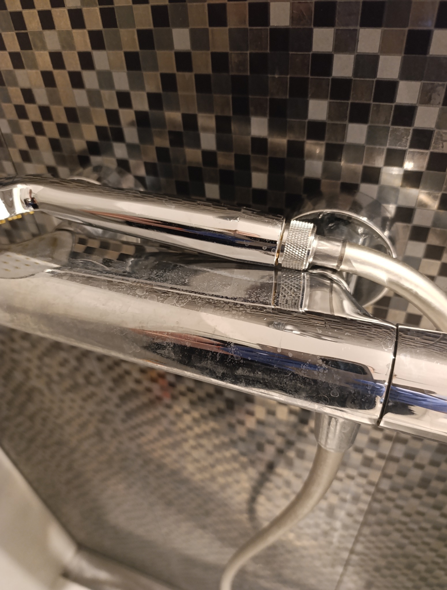 Zacieki i osad na chromowanej baterii prysznicowej na tle mozaiki. Bateria wymaga czyszczenia, widoczne ślady użytkowania i kamień.