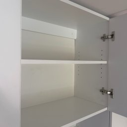 Niewczas Meble - Biała szafka z otwartymi drzwiami, ukazująca dwie regulowane półki, srebrne zawiasy i nowoczesny mechanizm push-to-open.