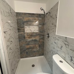 Life of Harmony art & design - Wykończona kabina prysznicowa z marmurowymi płytkami i wnęką, widok z toaletą. Uwagę przykuwa mozaika podłogowa i chromowana armatura.