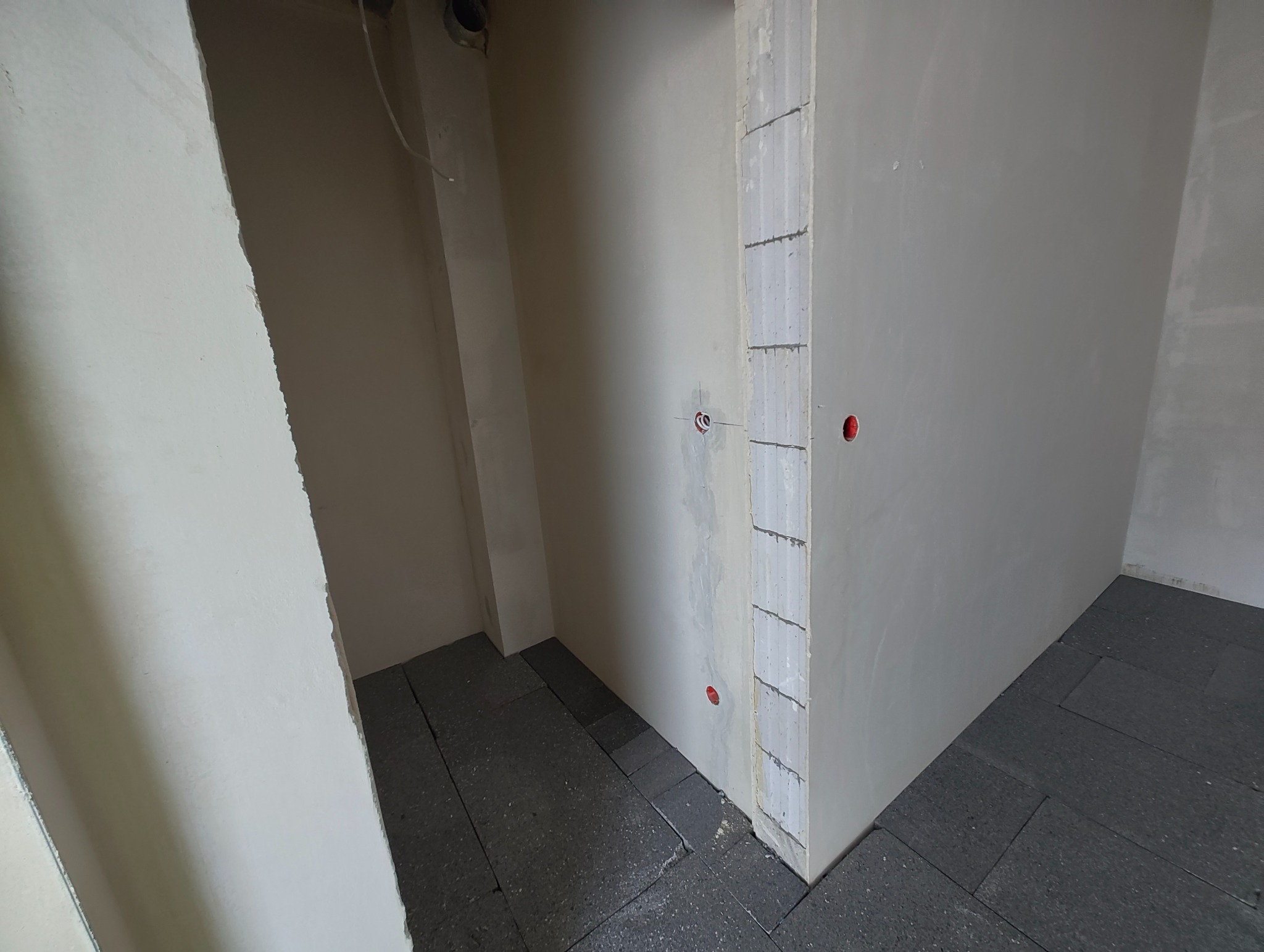 Surowy stan wnętrza z widocznymi punktami instalacji elektrycznej w ścianach i ułożoną izolacją podłogową, przygotowany do dalszych prac wykończeniowych.