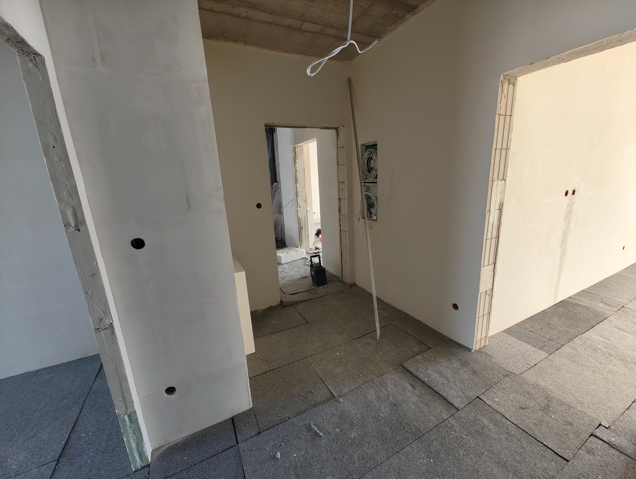 Wnętrze w trakcie remontu: surowy betonowy sufit, ściany po gładzi, przygotowane podłoże pod wylewkę, widoczne kable i puszki elektryczne. Stan deweloperski.