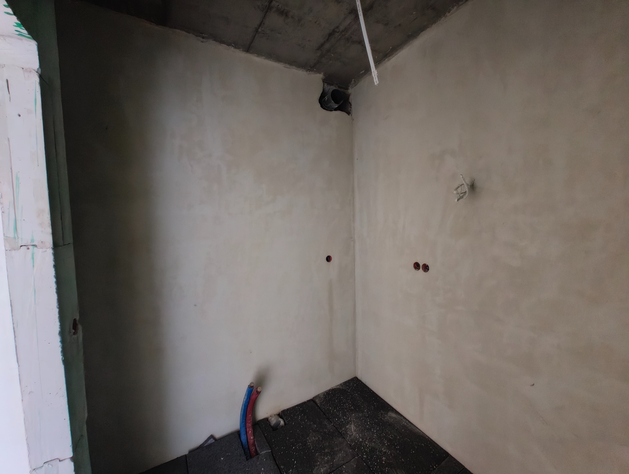 Surowy stan wnętrza z widocznymi przewodami i puszkami elektrycznymi w ścianach, przygotowany do dalszych prac wykończeniowych. Widoczny fragment instalacji wentylacyjnej.