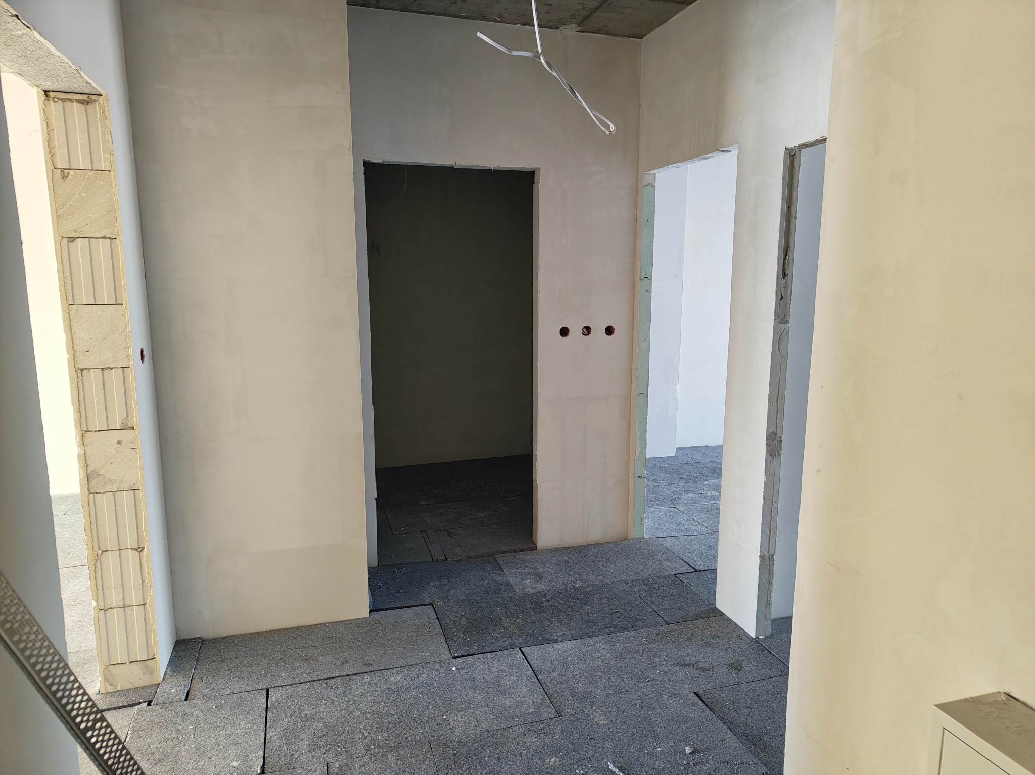 Wnętrze w trakcie remontu: surowe ściany z widocznymi przewodami, podłoga wyłożona płytami izolacyjnymi. Widoczne otwory na gniazdka elektryczne.