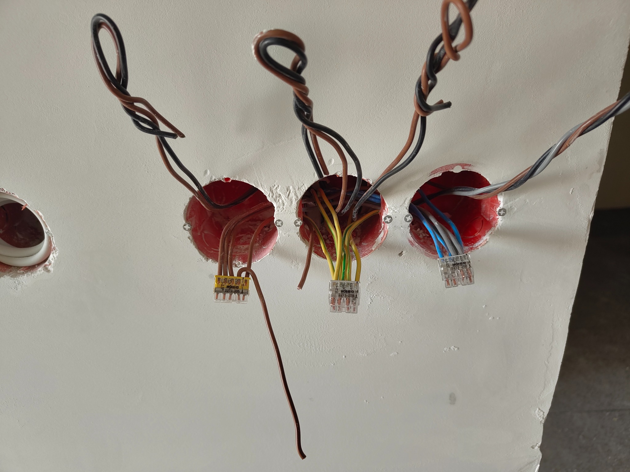 Przygotowane otwory w suficie z wystającymi przewodami i złączkami WAGO, gotowe do montażu oświetlenia. Widoczne kolory przewodów i detale złączek.