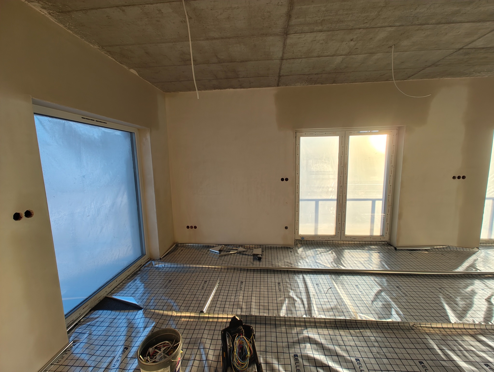 Wnętrze w trakcie prac wykończeniowych: widoczne kable wystające z sufitu, puszki elektryczne w ścianach i rozłożona mata grzewcza na podłodze.