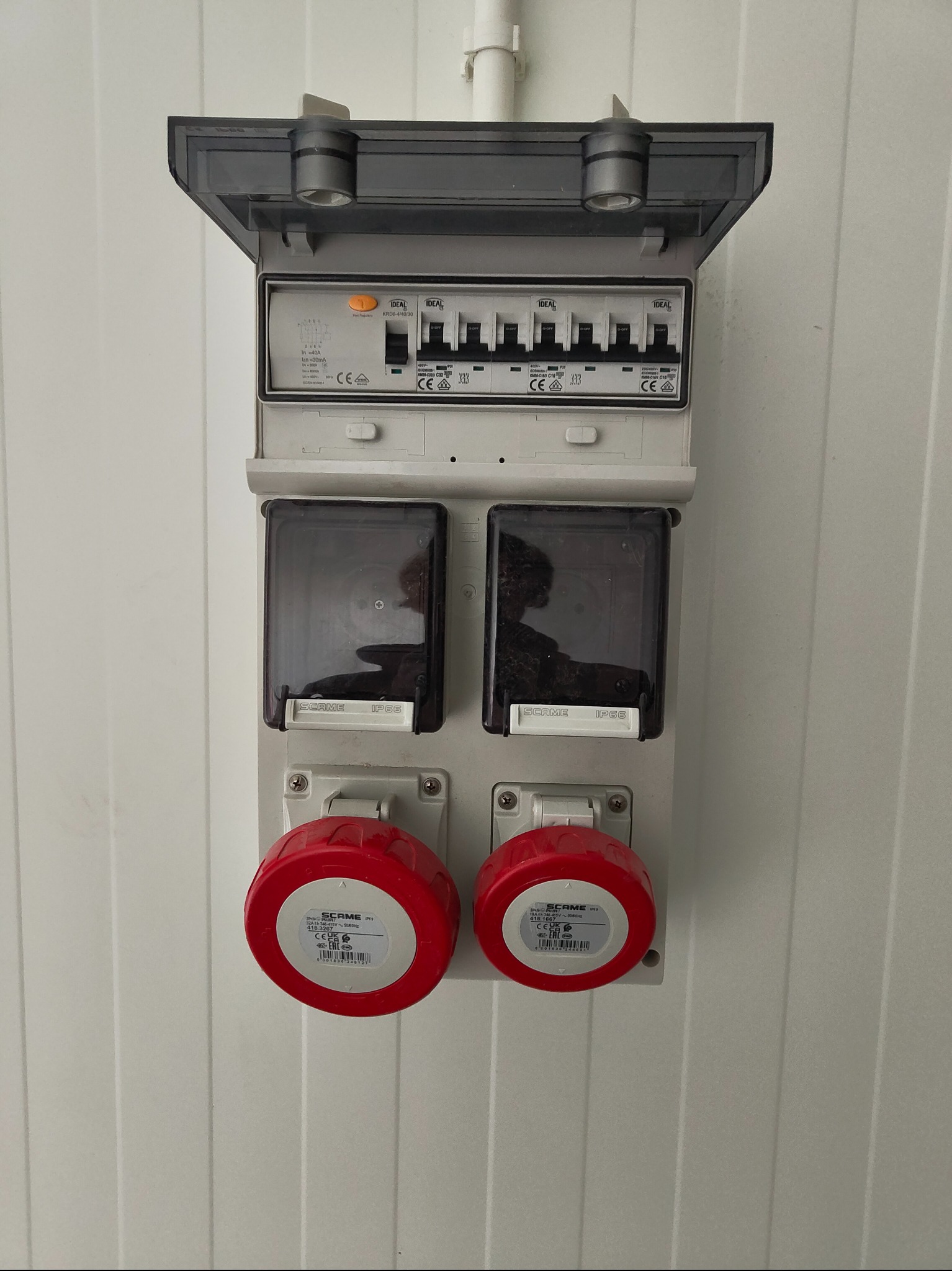 Rozdzielnica elektryczna z wyłącznikami i gniazdami przemysłowymi SCAME, zamontowana na białej ścianie z paneli. Widoczne zabezpieczenia i oznaczenia.