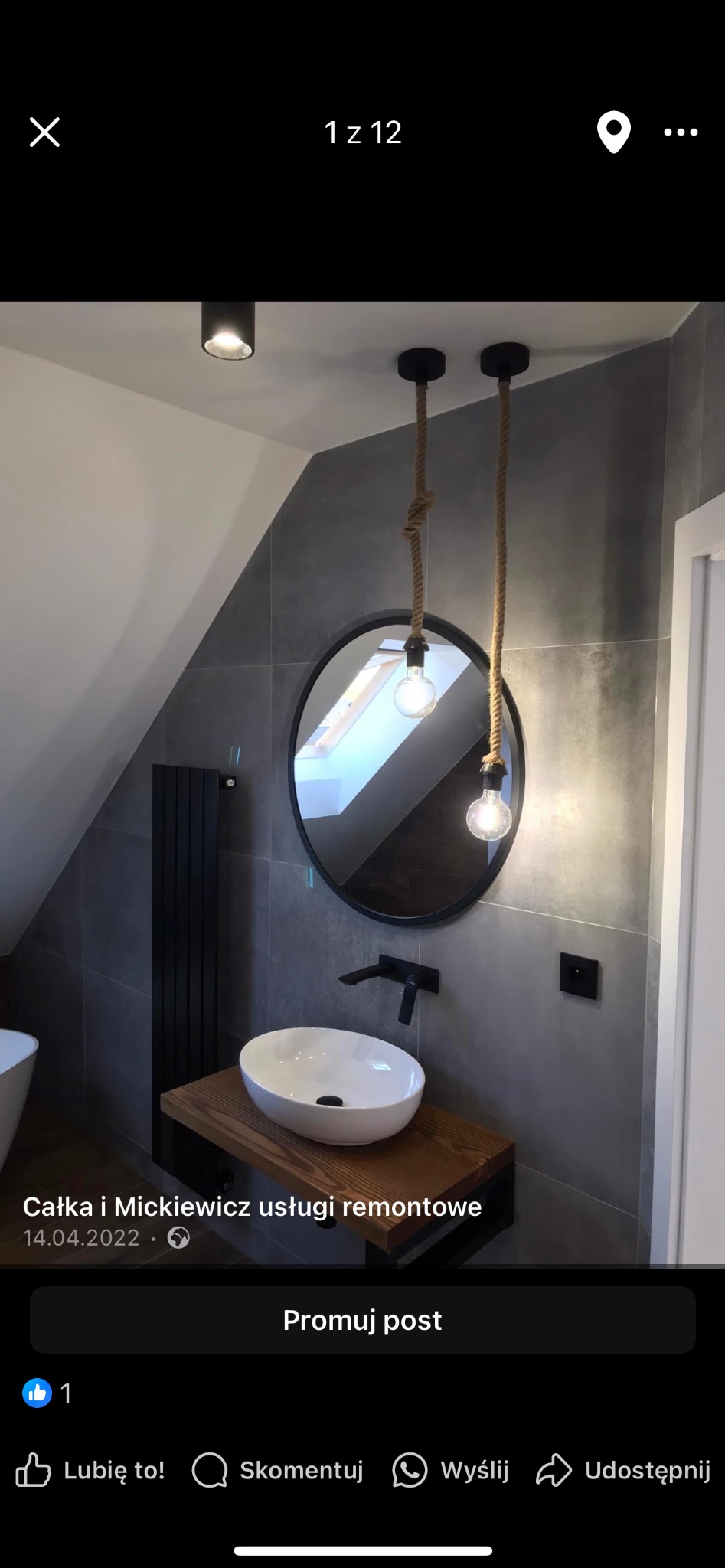 Nowoczesna łazienka na poddaszu z owalną umywalką na drewnianym blacie, okrągłym lustrem i lampami na sznurach. Szare płytki, czarne akcenty.