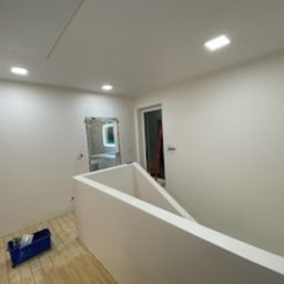 Prywatno - Białe, świeżo pomalowane wnętrze z widoczną barierką i podłogą z jasnego drewna. W tle łazienka z lustrem i oknem.