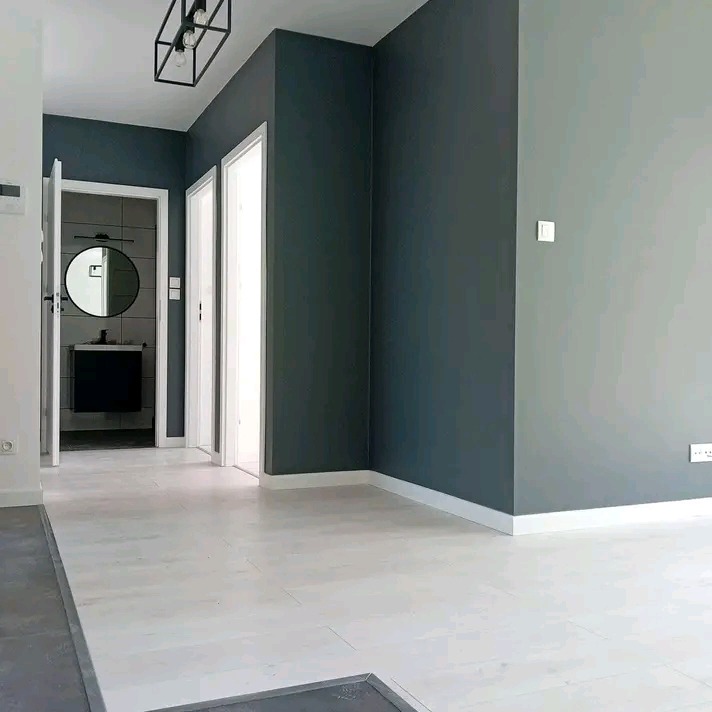 Nowoczesne wnętrze po malowaniu ścian na szaro i grafitowo, z białymi listwami przypodłogowymi i podłogą. Widok na łazienkę z okrągłym lustrem.