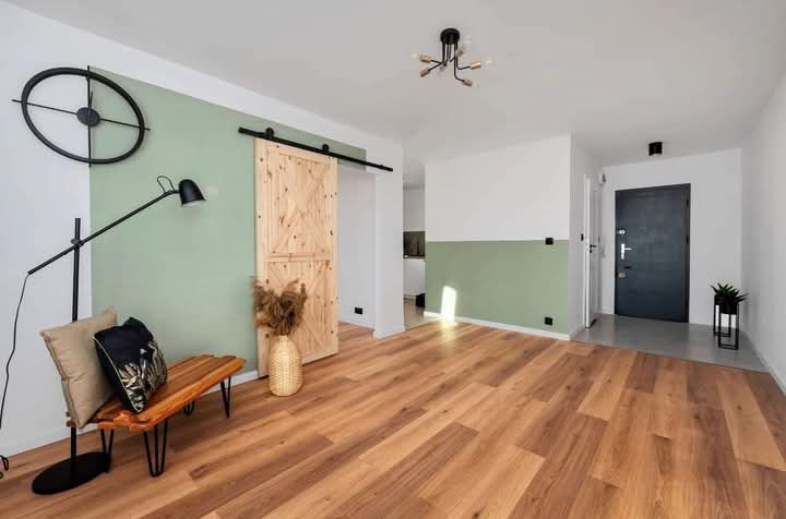 Nowoczesne wnętrze: drewniana podłoga, ściany w dwóch odcieniach zieleni i bieli, przesuwne drzwi stodołowe i dekoracje w stylu skandynawskim.