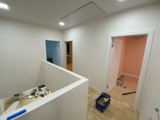 Białe wnętrze po remoncie: świeżo pomalowane ściany, widoczne wejścia do pomieszczeń, fragment schodów i podłogi. Minimalizm i czystość.