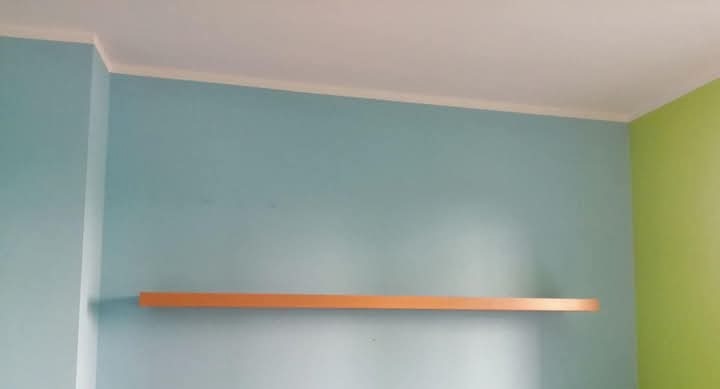 Pomalowany na błękitno pokój z zielonym akcentem, listwą przypodłogową i półką z jasnego drewna, umieszczoną w dolnej części kadru.