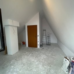 Hubert Kwiatkowski - Białe poddasze po szpachlowaniu, widoczne worki z zaprawą, drabiny i świeżo pomalowane ściany. Przygotowanie do dalszych prac wykończeniowych.