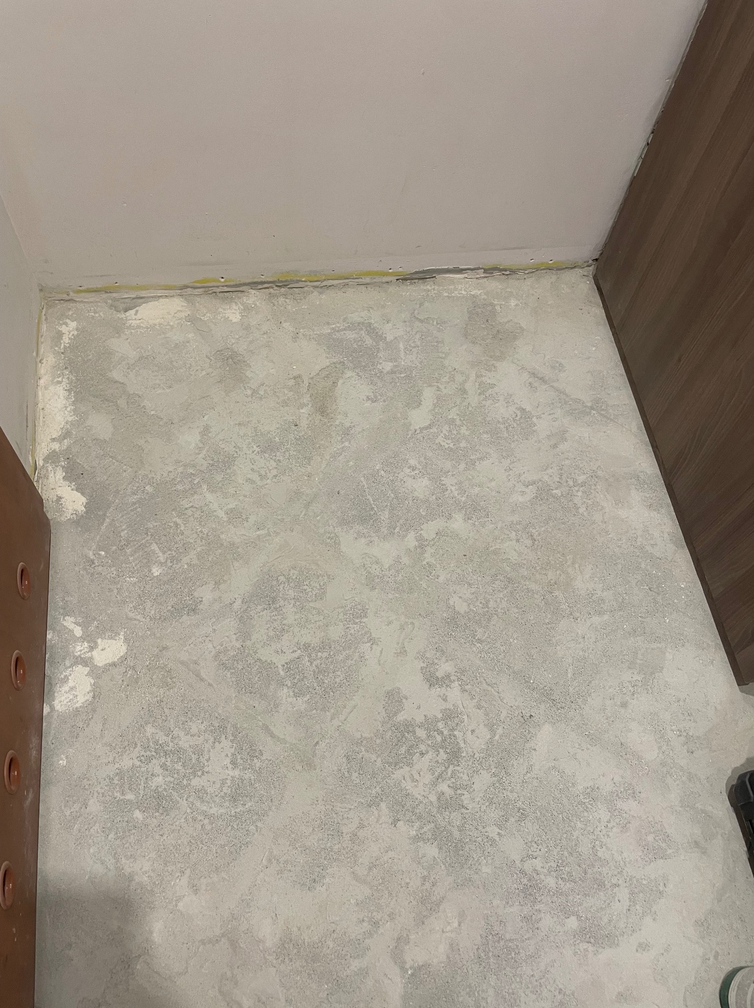 Przygotowane podłoże pod panele: wyrównana, szpachlowana podłoga w rogu pomieszczenia, widoczne ślady po szpachlowaniu, listwa przypodłogowa wzdłuż ściany.