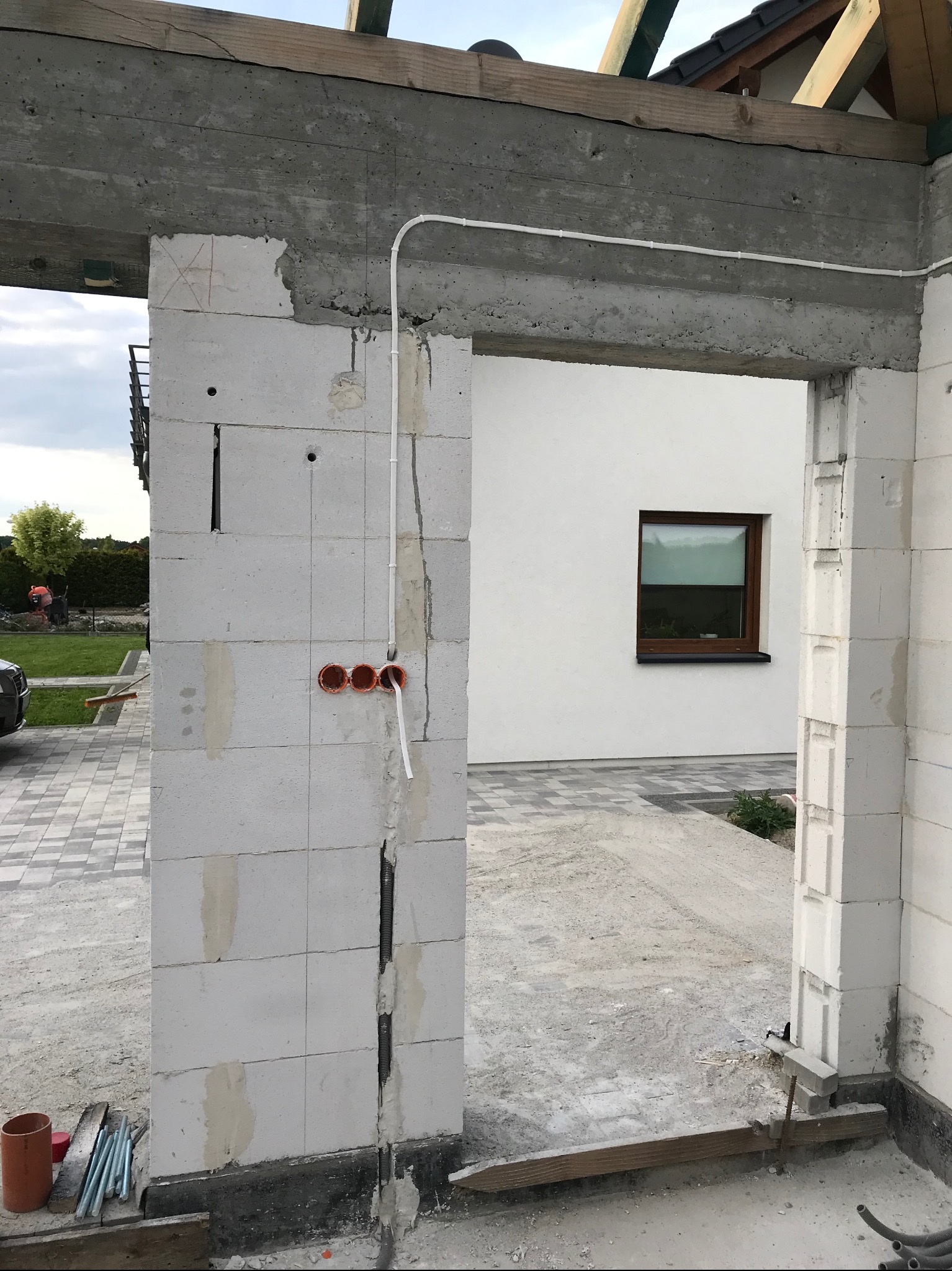 Wewnętrzna instalacja elektryczna w surowym stanie: widoczne puszki i kable w ścianie z betonu komórkowego. Budynek w trakcie budowy, okno w tle.