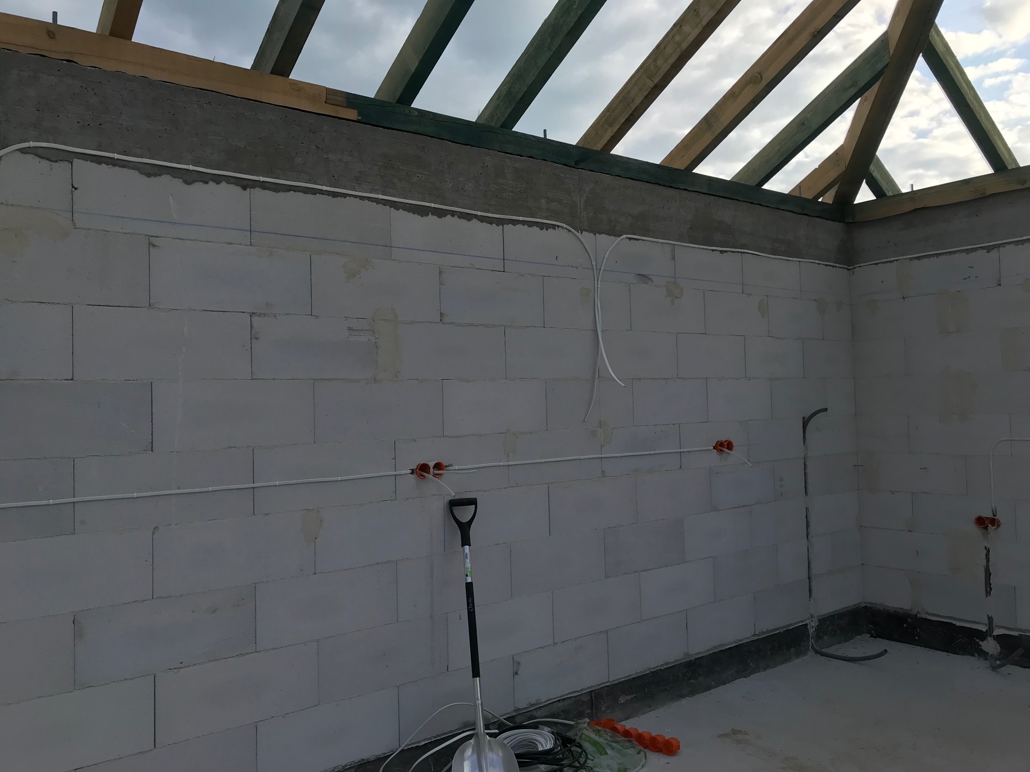 Wnętrze w trakcie budowy z widocznymi przewodami elektrycznymi poprowadzonymi po ścianach z betonu komórkowego i elementami instalacji pod sufitem.